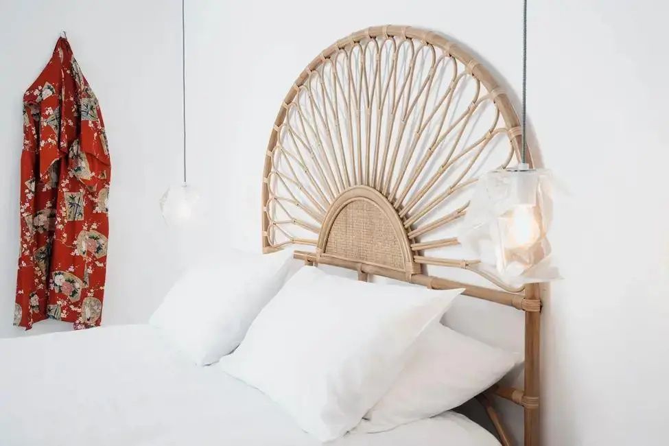 Doppelbett mit weißen Kissen und einem Kopfteil aus hellem Rattan.