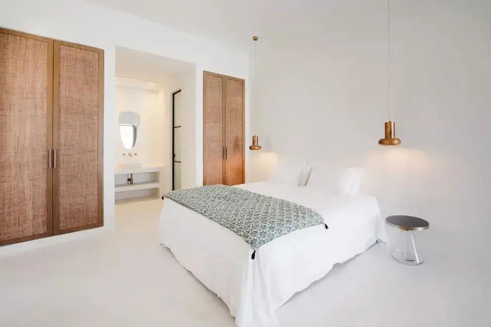 Weiß eingerichtetes Schlafzimmer mit Doppelbett, Holzschrank und Blick auf den Waschtisch