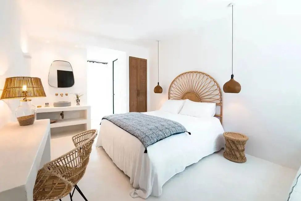 Weißes Hotelzimmer mit Doppelbett, Rattan-Kopfteil, Hängelampen und integriertem Waschtisch.