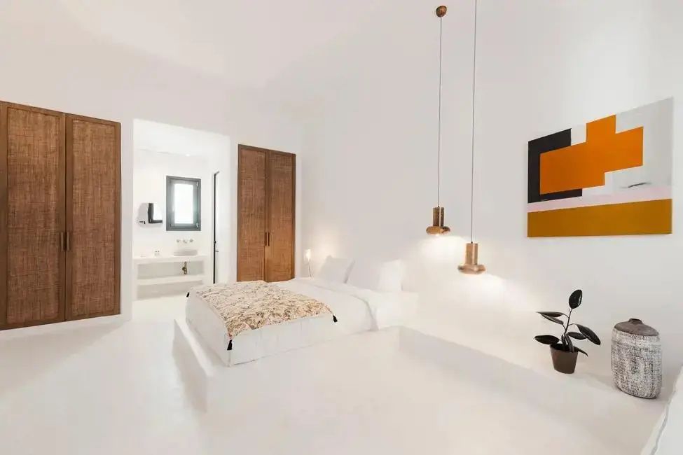 Minimalistisches weißes Hotelzimmer mit Doppelbett, Hängeleuchten und integrierter Waschnische.
