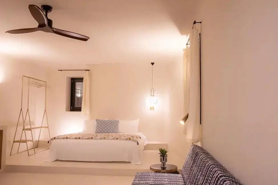 Weißes Hotelzimmer bei warmem Licht mit großem Doppelbett und einem Sofa.