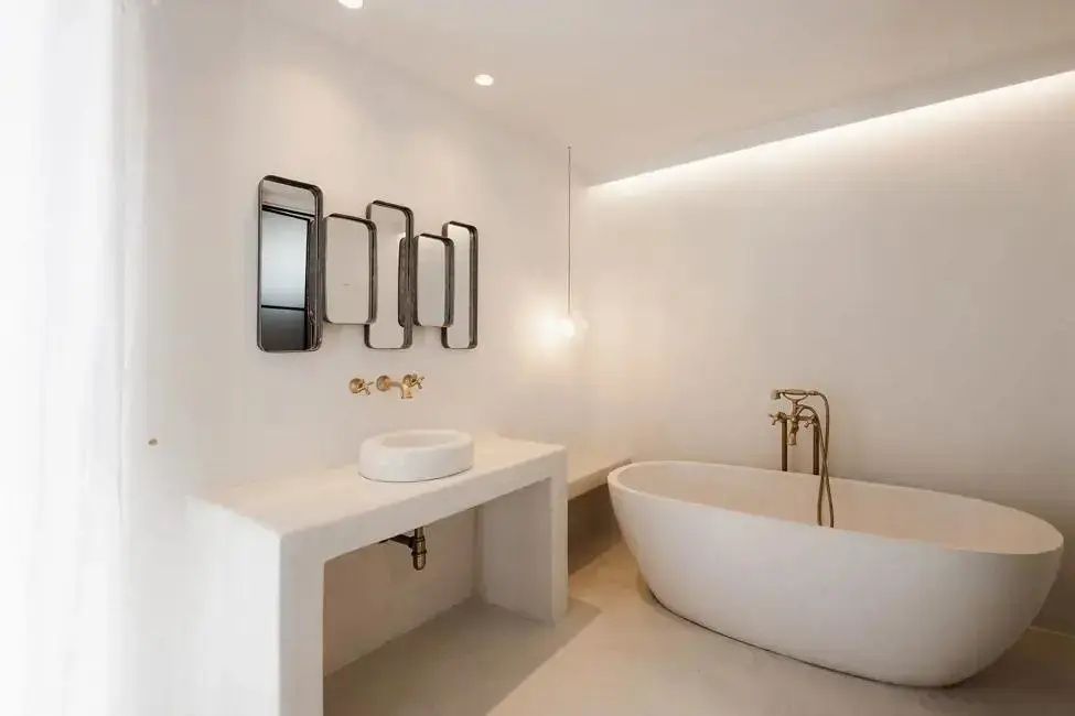 Helles Badezimmer mit freistehender Badewanne, weißem Waschtisch und wandmontierten Spiegeln.