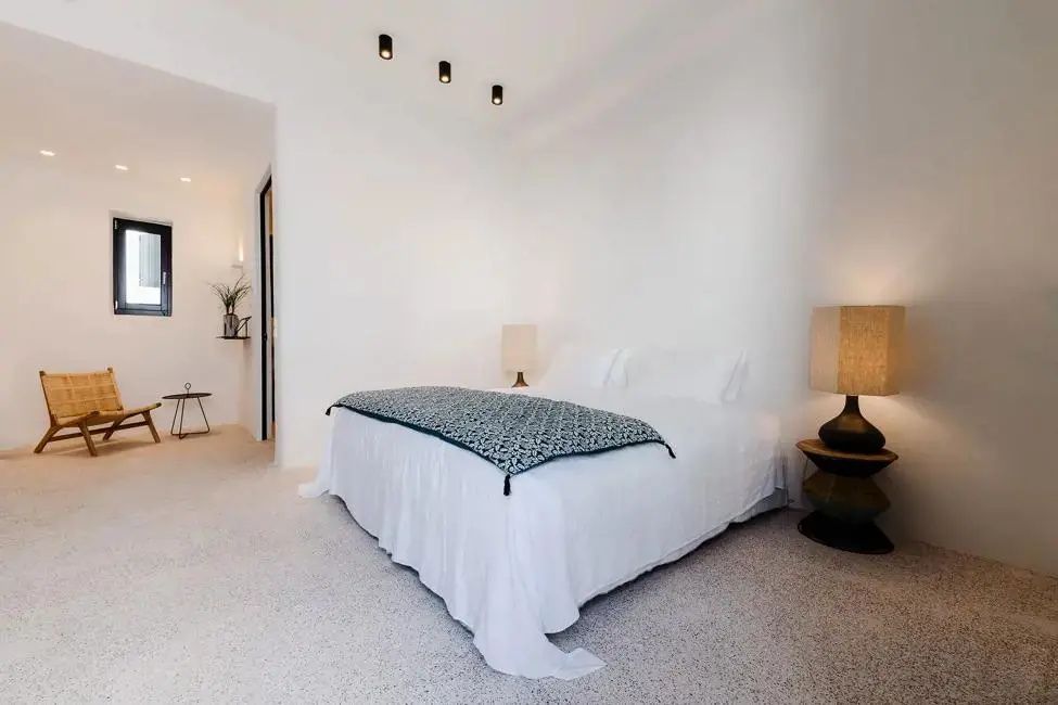 Helles Schlafzimmer mit weiß bezogenem Doppelbett, einer gemusterten Tagesdecke und Nachttischlampen.