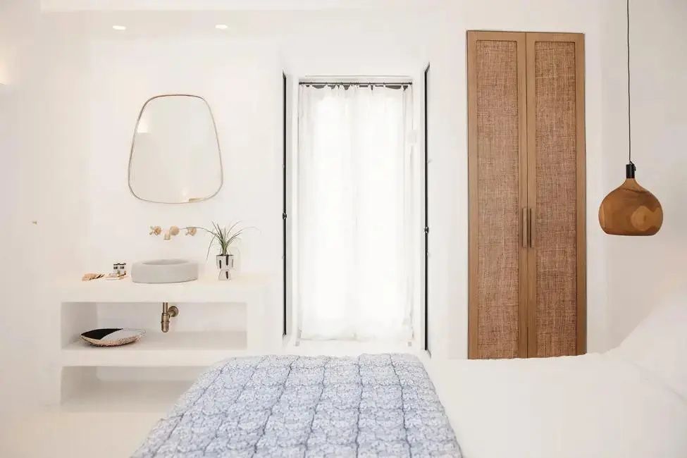 Blick über das Bett auf den integrierten Waschtisch, den Spiegel und einen Einbauschrank.