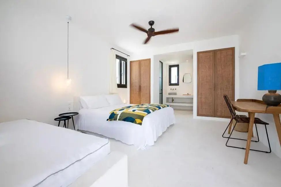 Helles Hotelzimmer mit Doppelbett, Holzschränken, weissem Boden und Ventilator an der Decke.