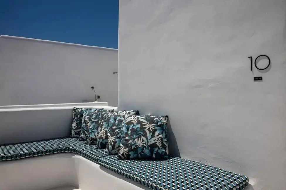 Sitzbank auf einer weißen Terrasse mit blau gemusterten Kissen unter blauem Himmel.