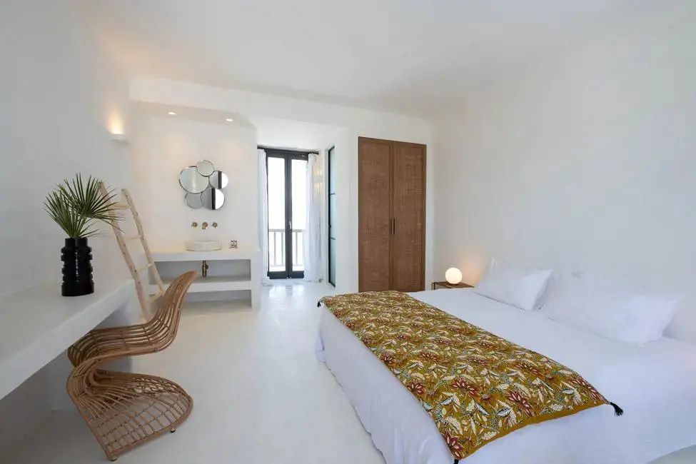 Großzügiges weißes Zimmer mit Doppelbett, Sitzbereich, Waschtisch und Ausgang zum Balkon.