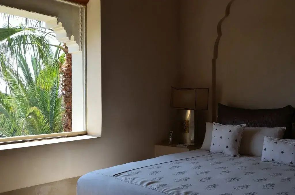 Schlafbereich mit weißem Bett und einem Fenster mit Blick in den Garten.