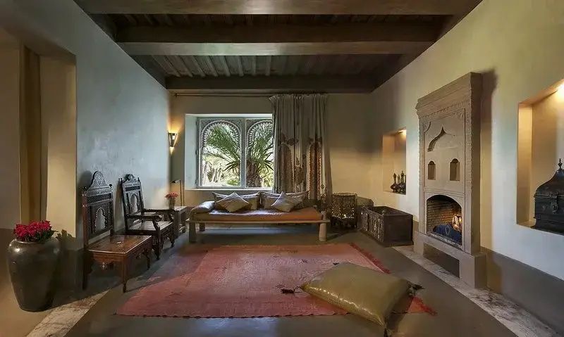 Wohnbereich mit Tagesbett, Teppich, Holzstuhl und Kamin unter einer dunklen Holzdecke.