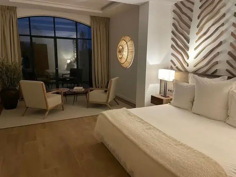 Geräumiges Hotelzimmer mit hellen Möbeln, Sitzbereich und großer Fensterfront.