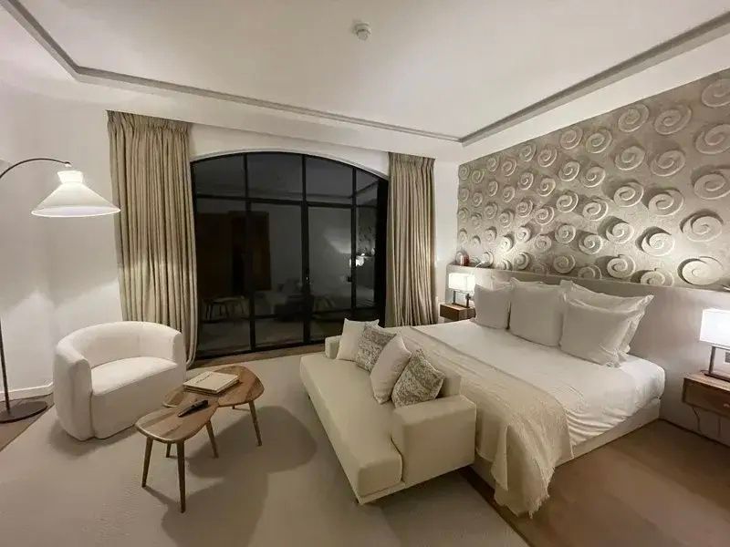 Schlafzimmer bei Nacht mit Doppelbett, weißem Sofa und strukturierter Wandgestaltung.