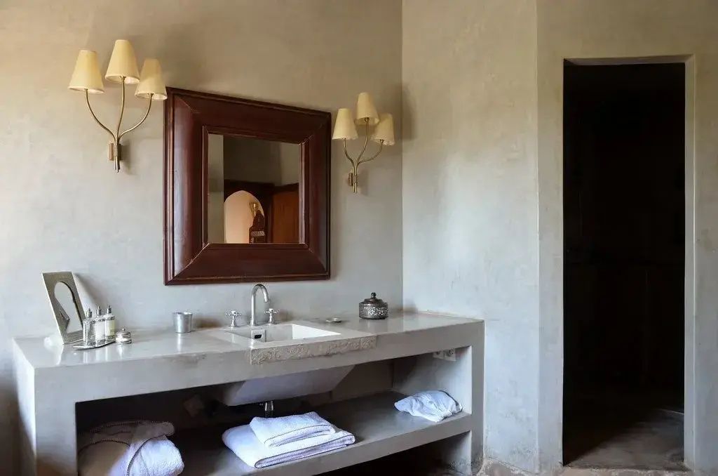 Badezimmer mit Waschtisch aus Stein, Spiegel und zwei Wandlampen.