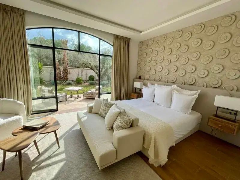 Helles Hotelzimmer mit Doppelbett, Sofa und geöffneter Fenstertür zum Garten.