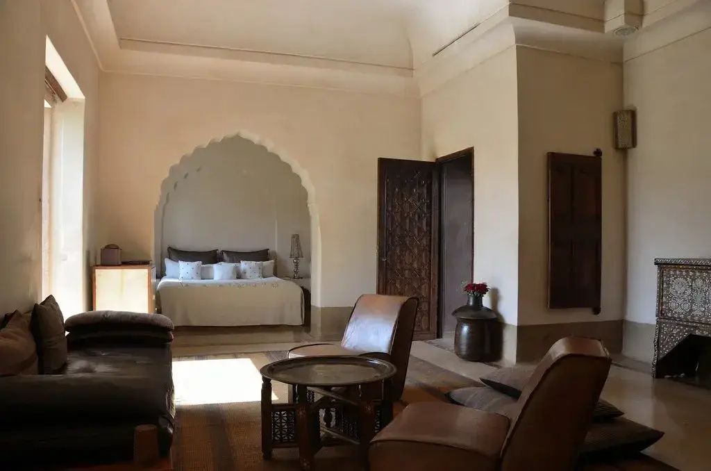 Sitzbereich mit Ledersesseln und einem runden Metalltisch vor dem Bett in einer Bogennische.