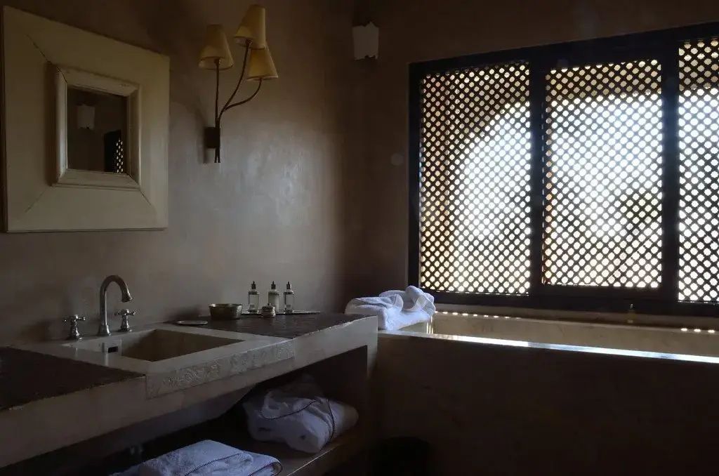 Badezimmer mit steinerner Waschanlage und einem traditionellen Holzgitterfenster.