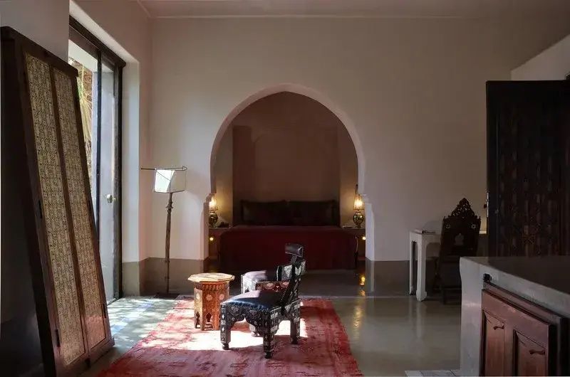 Zimmer mit orientalischem Stuhl, rotem Teppich und Bett im Rundbogen.