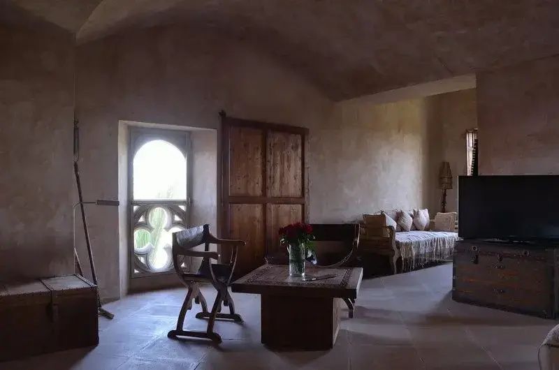 Wohnbereich einer Suite mit Gewölbedecke, Holztisch, Stuhl und Blick auf ein verziertes Fenster.