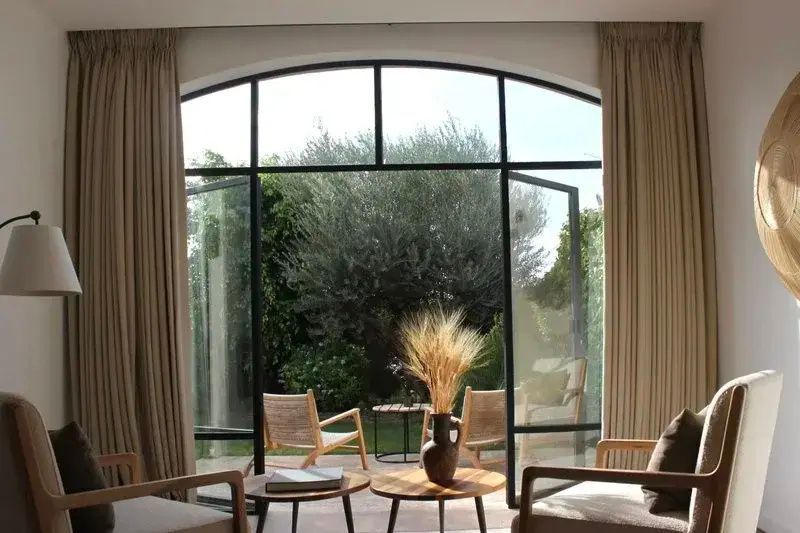 Blick durch ein großes Bogenfenster auf eine grüne Terrasse mit Gartenmöbeln.