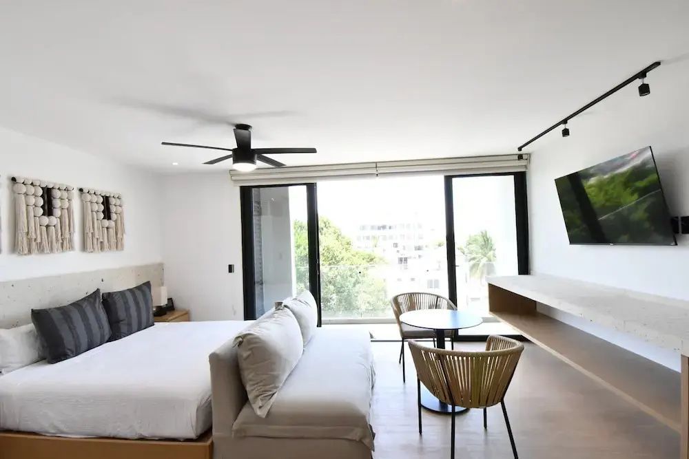 Schlafbereich der Suite mit Doppelbett, Sofa und großen Fenstern mit Ausblick ins Grüne.