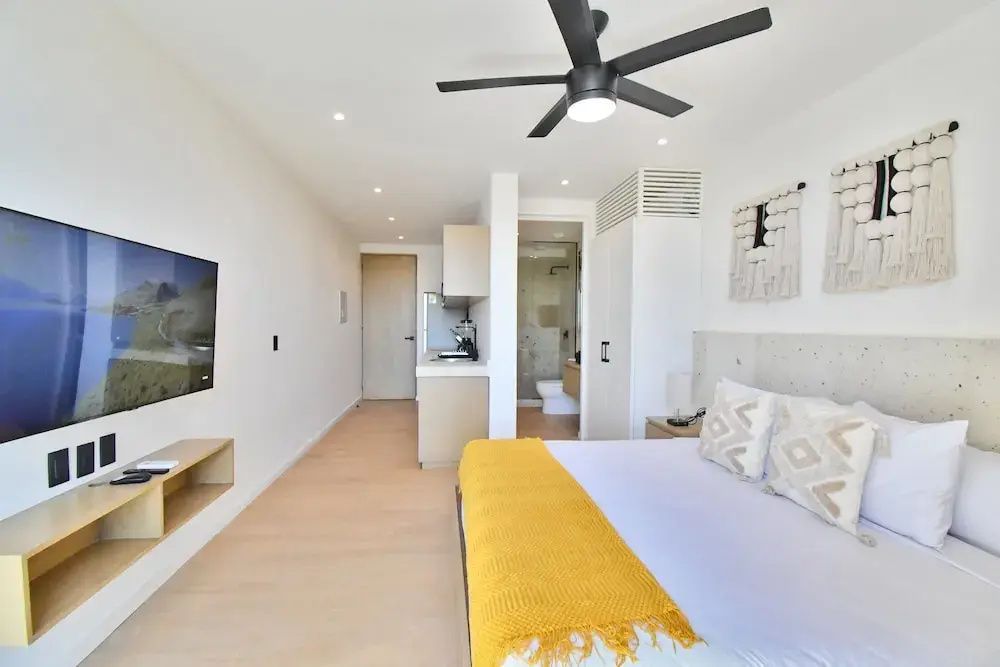 Schlafbereich mit Doppelbett, gelbem Überwurf, Deckenventilator und Blick zum Flur.