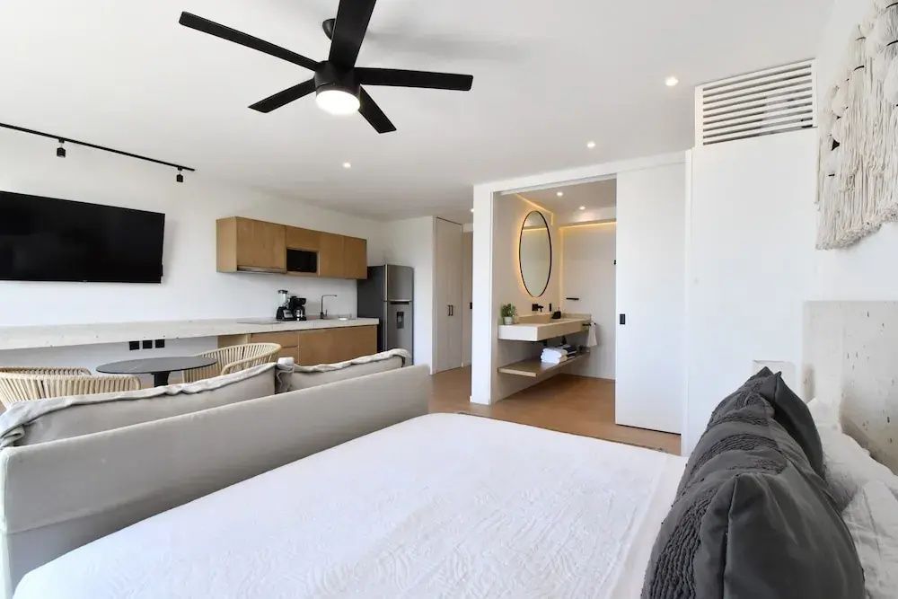 Blick über das Bett auf den offenen Küchenbereich und das Badezimmer mit beleuchtetem Spiegel.