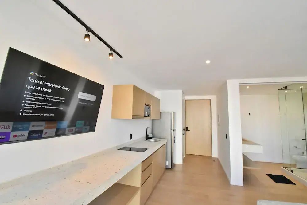 Küchenzeile aus Holz mit Fernseher an der Wand, Kühlschrank und hellem Boden im Appartement.