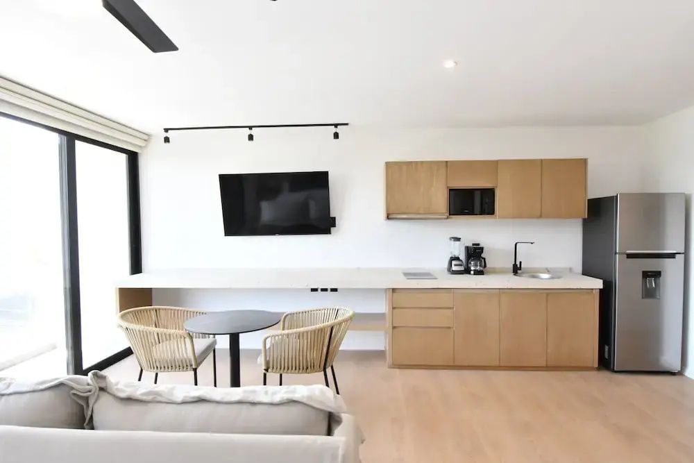 Küchenzeile aus Holz mit Küchengeräten, Flachbildfernseher und rundem Esstisch für zwei Personen.