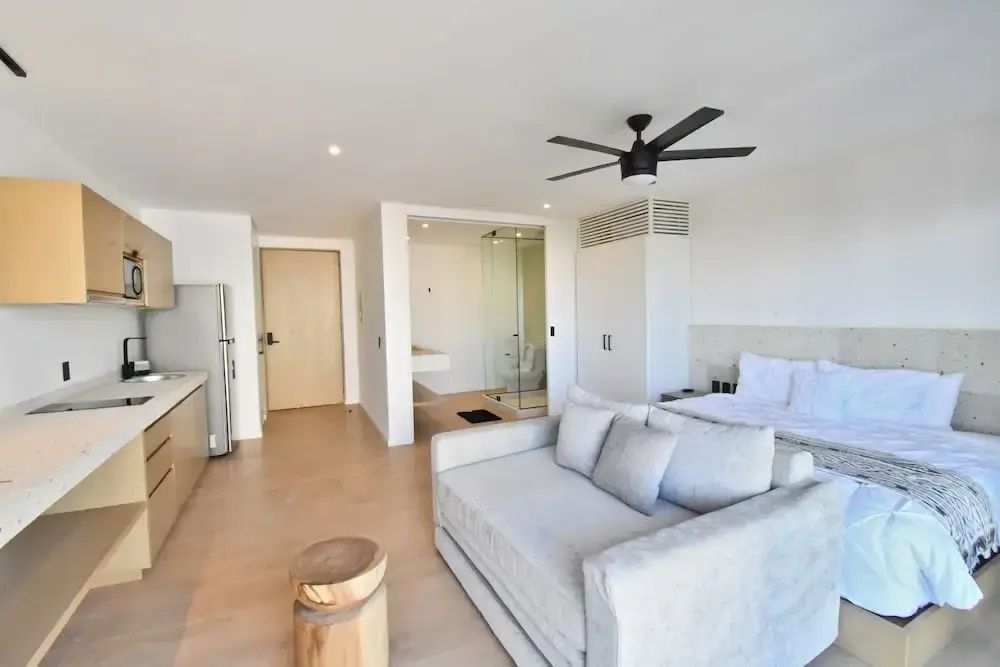 Helles Zimmer mit Doppelbett, beigem Sofa, Holz Beistelltisch und durchsichtigem Badbereich.
