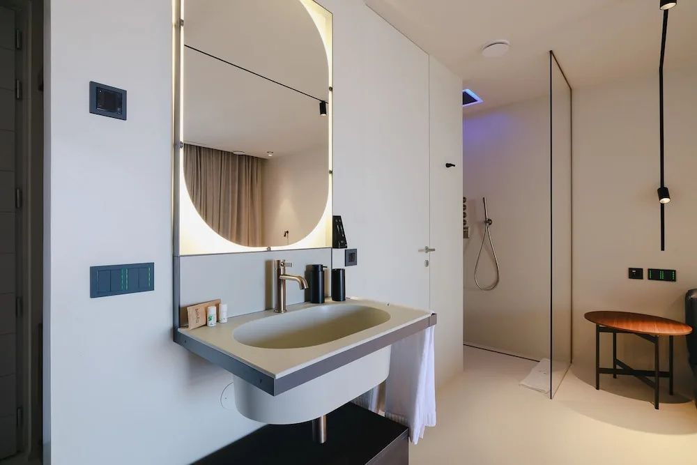 Waschbecken mit beleuchtetem Spiegel und Blick auf die angrenzende Dusche.
