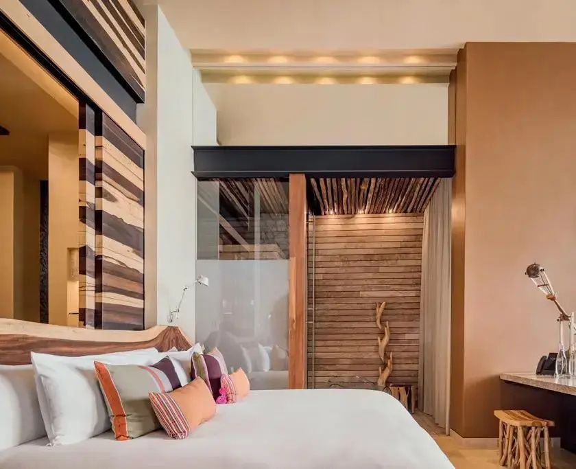Hotelzimmer mit Doppelbett, farbigen Kissen und Holzvertäfelung an den Wänden.