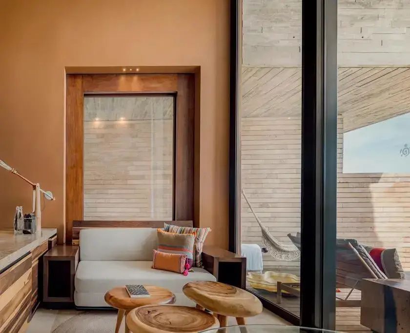 Sitzbereich im Hotelzimmer mit einer hellen Couch, Holztischen und Blick auf die Terrasse.