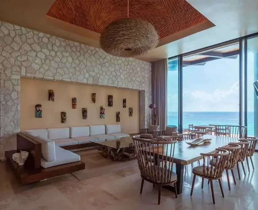 Geräumiges Wohnzimmer mit Holztisch, großem Sofa und Blick auf das Meer durch Glasfronten.