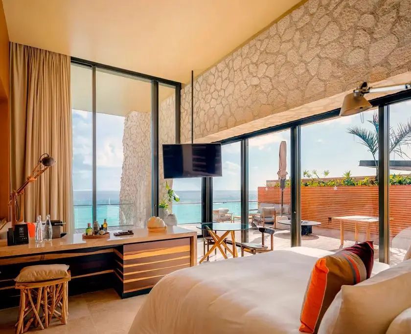 Hotelzimmer mit großem Bett, Schreibtisch und bodentiefen Fenstern mit Meerblick.