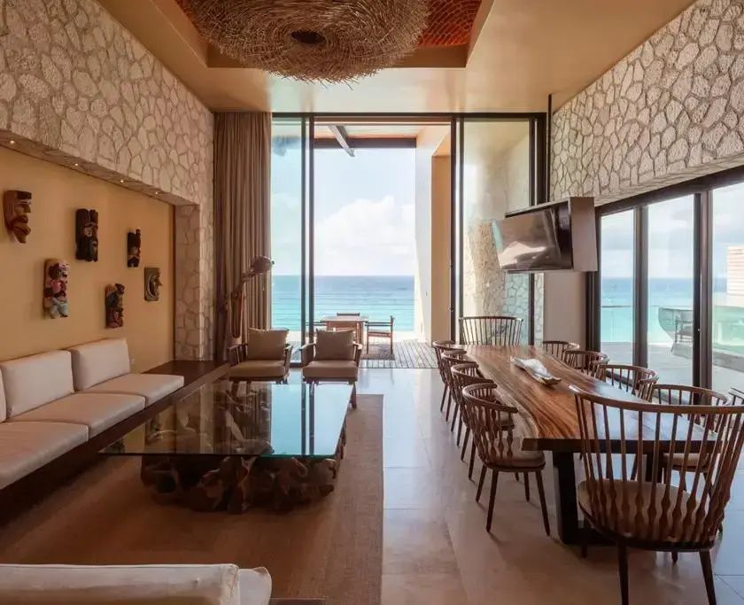 Großer Loungebereich mit Massivholztisch, Sitzecke und Panoramafenstern mit Blick aufs Meer.