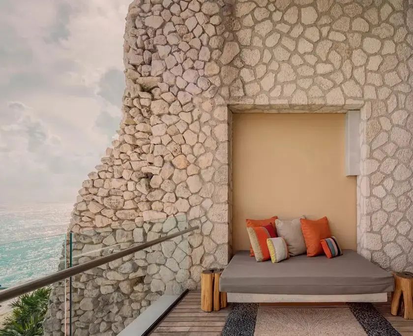 Überdachter Balkon mit Liegebett, bunten Kissen und Blick auf den Ozean.