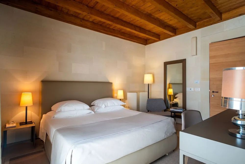 Schlafzimmer mit Holzbalkendecke, großem Doppelbett, Nachttischlampen und Spiegel.