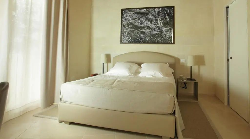 Modernes Hotelzimmer mit großem Doppelbett, Wandbild, beigefarbenen Wänden und Nachttischlampen.