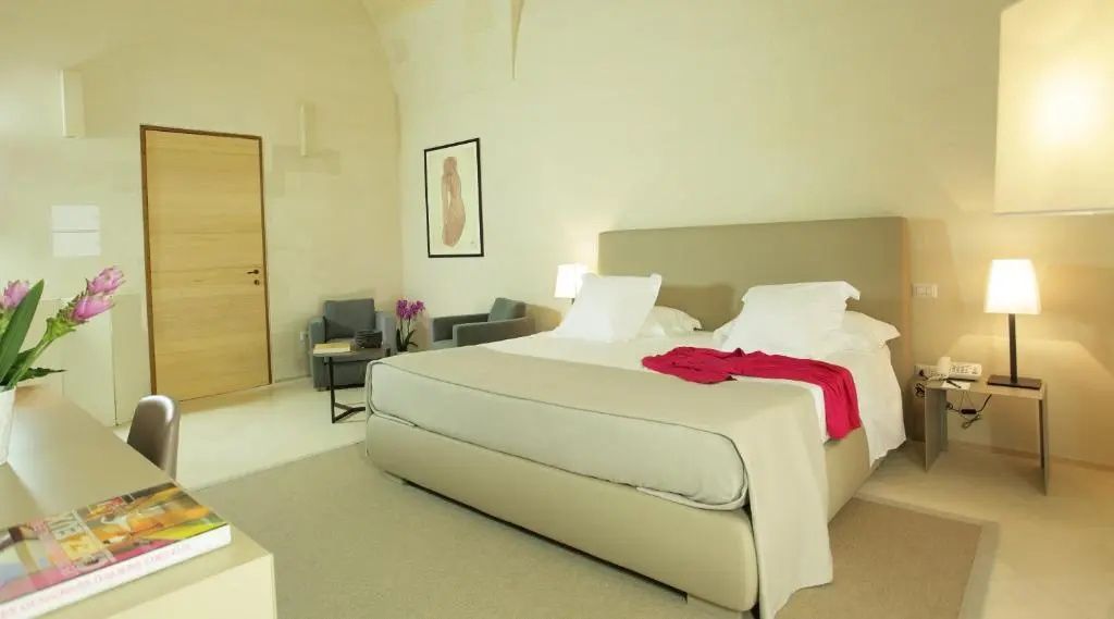 Modernes Hotelzimmer mit einem großen Doppelbett, hellem Teppich und Sitzgelegenheiten im Hintergrund.