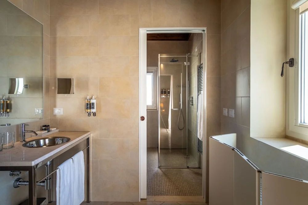 Badezimmer mit Sandsteinwänden, Waschtisch und Blick auf die abgegrenzte Dusche.