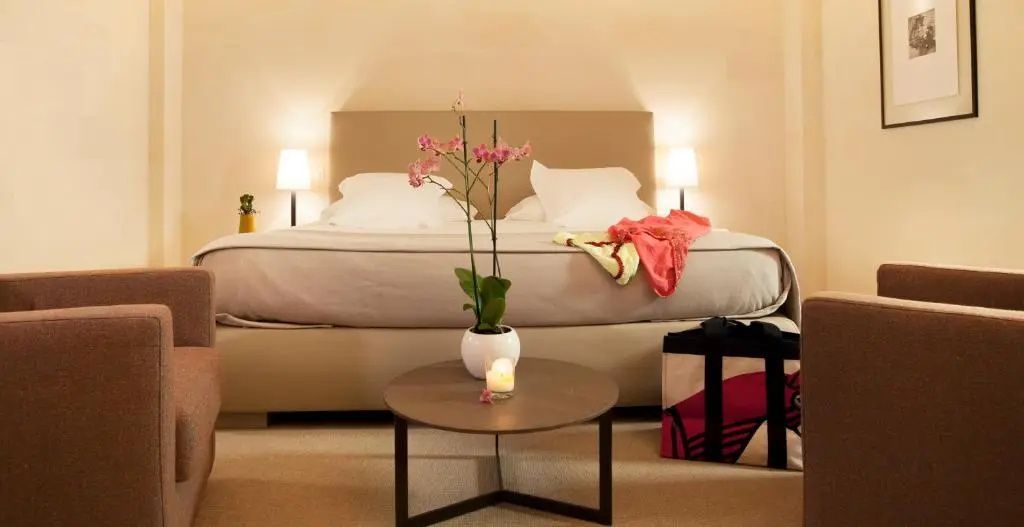 Doppelbett mit beigefarbenem Kopfteil, Nachttischlampen und ein kleiner Tisch mit Orchidee davor.