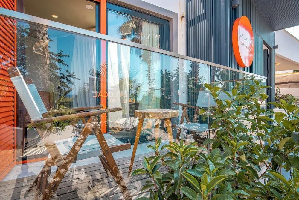 Balkon mit Glasgeländer, einem Holztisch und Stühlen vor der Zimmerfront.