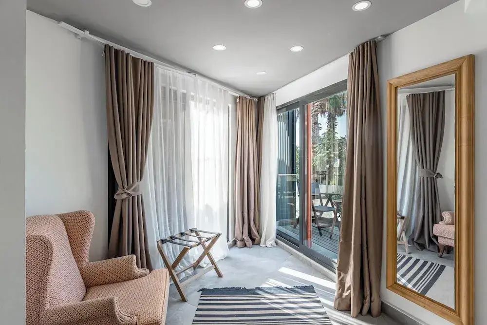 Sitzbereich im Hotelzimmer mit bodentiefen Vorhängen, Sessel und Zugang zur Terrasse.