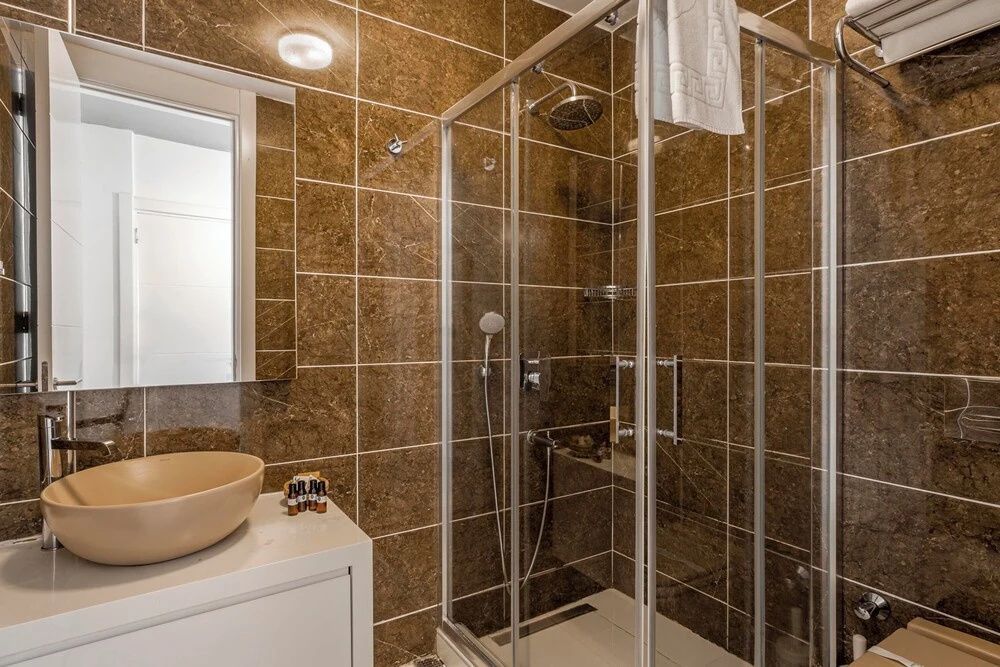 Badezimmer mit braunen Wandfliesen, Glaskabine für die Dusche und Waschtisch.