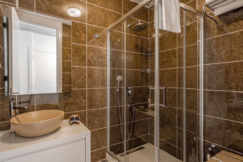 Badezimmer mit braun gefliesten Wänden, Duschkabine aus Glas und Aufsatzwaschbecken.