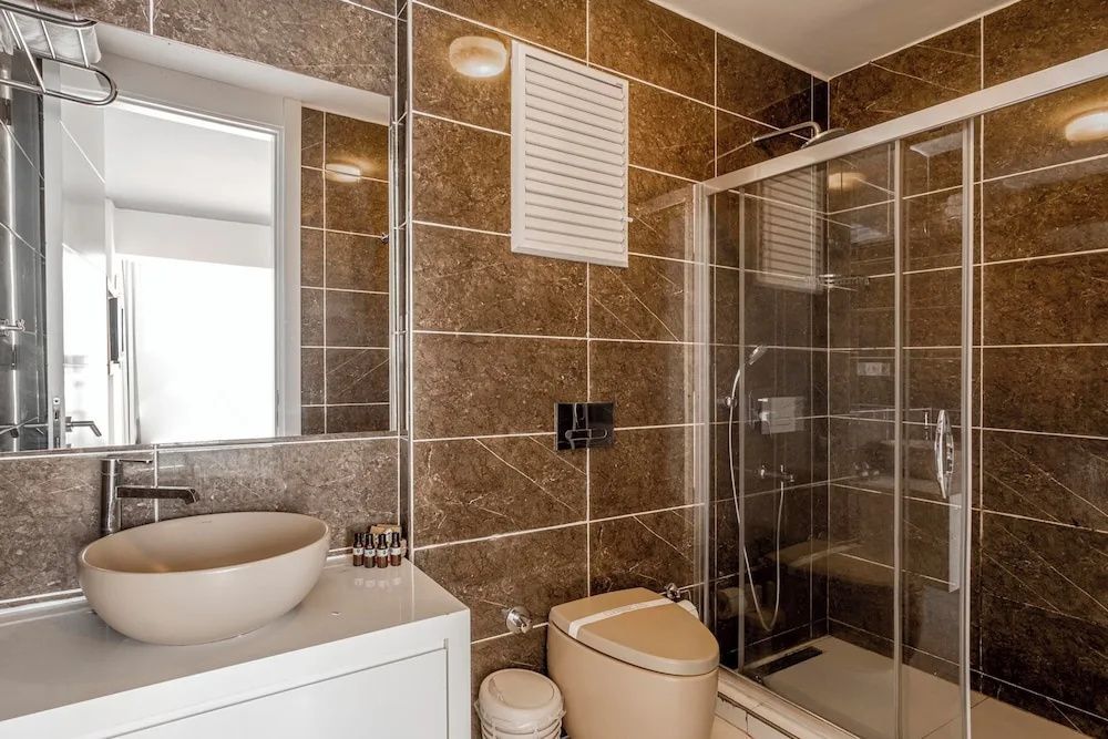 Badezimmer mit braun gefliesten Wänden, WC, Aufsatzbecken und Duschkabine.