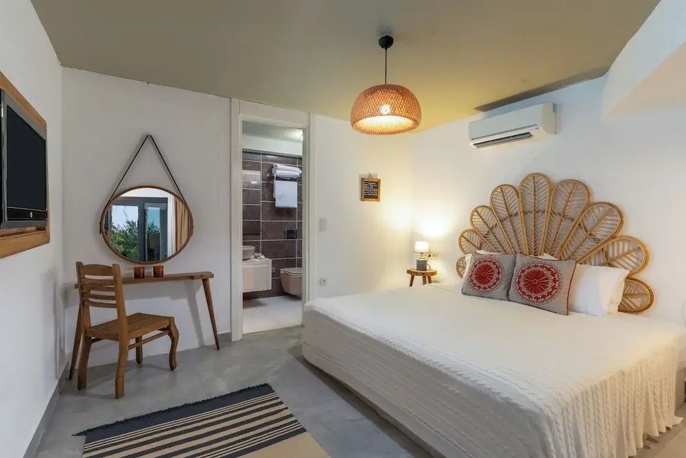 Schlafzimmer mit fächerförmigem Kopfteil aus Rattan, Schminktisch, Rundspiegel und Badzugang.