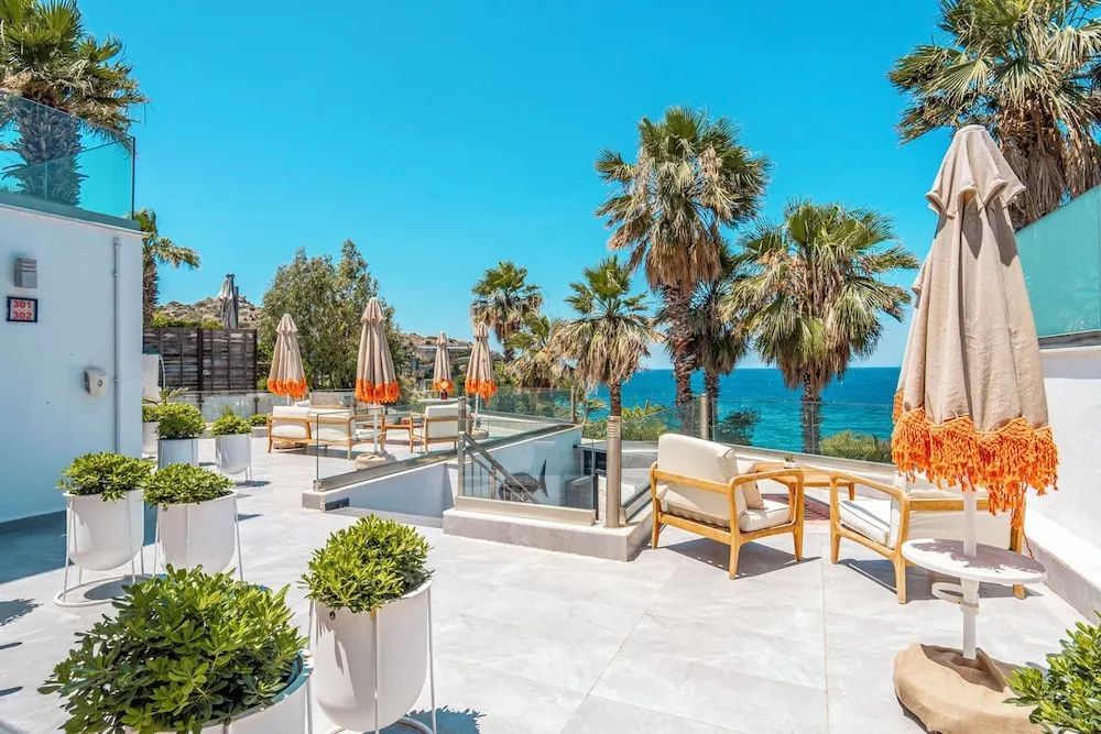 Terrasse mit Liegestühlen, Sitzgelegenheiten, Palmen und Ausblick auf das Meer.