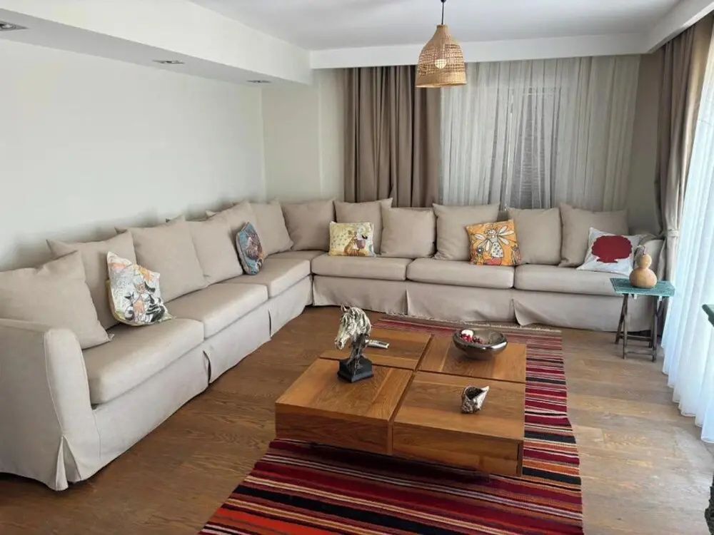 Geräumiger Wohnbereich mit großer Eckcouch, Holztisch und buntem Teppich.