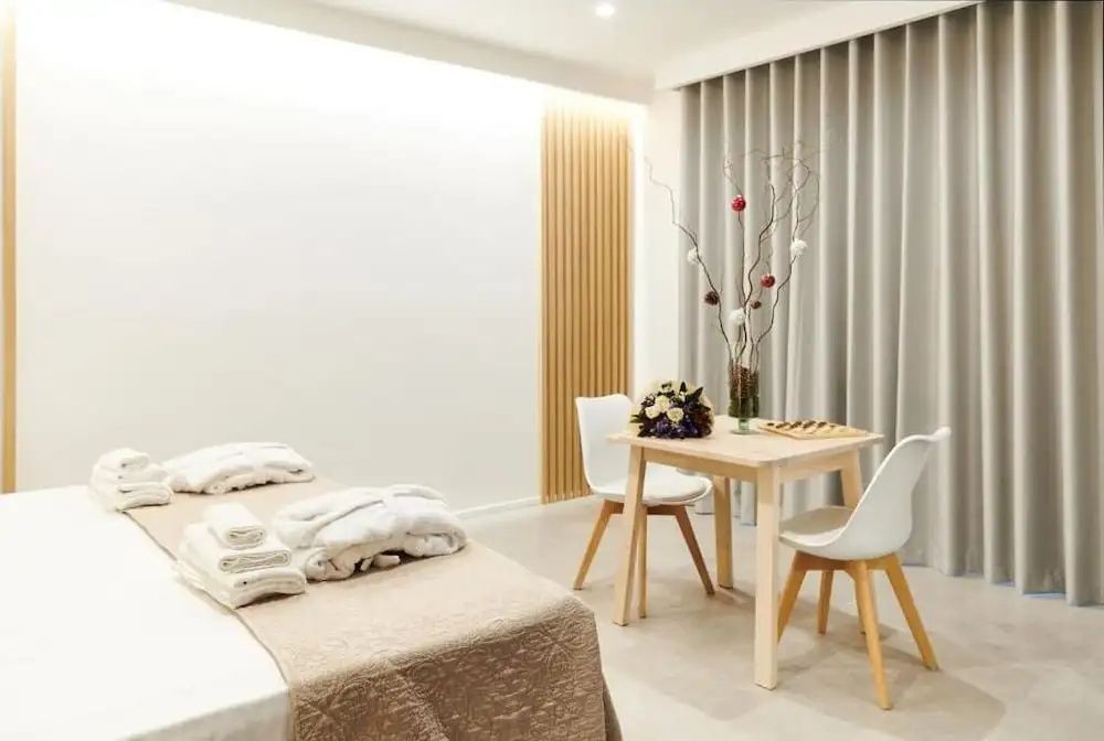 Helles Hotelzimmer mit Doppelbett, Bademänteln, kleinem Holztisch und zwei Stühlen.
