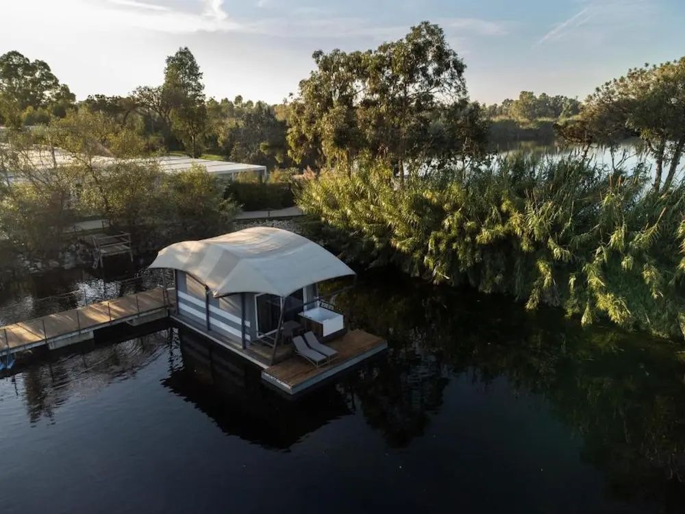 Schwimmende Unterkunft auf einem See mit Holzdeck, Sonnenliegen und Whirlpool am Ufer.
